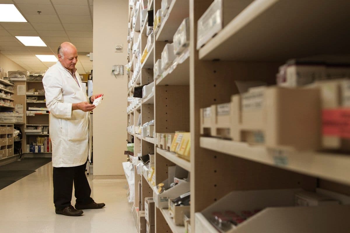 A pharmacist beside a shelf of medicines